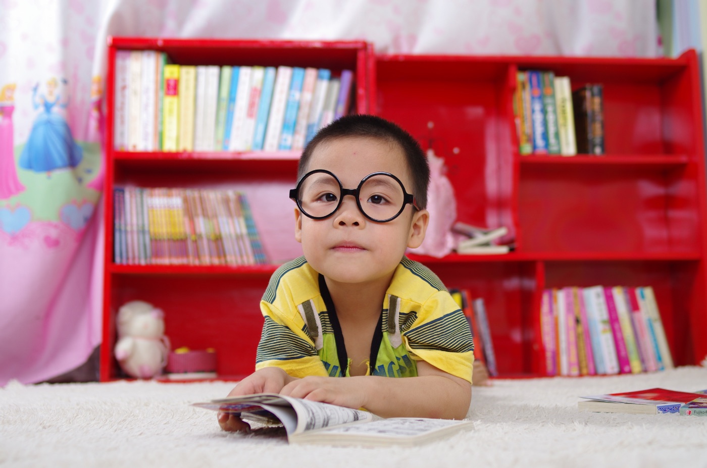 A child reading on the floor wearing glasses